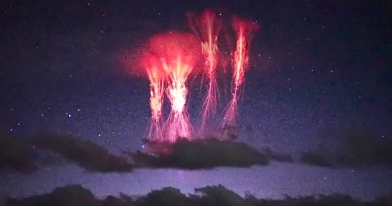 Bright red lightning-like sprites appear above dark clouds in the night sky, with stars faintly visible in the background. The glowing red tendrils stretch vertically, creating an ethereal effect.