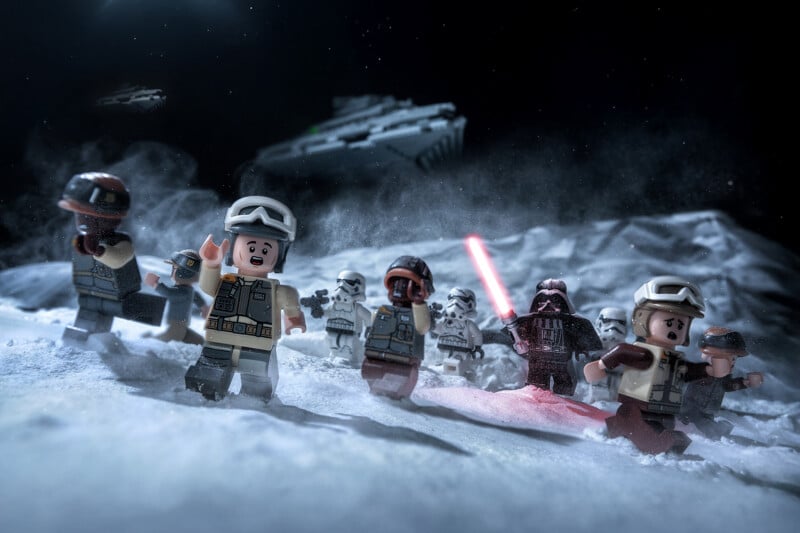 LEGO Star Wars minifigures, including Rebel soldiers and Darth Vader with a red lightsaber, are battling on a snowy landscape with an Imperial Star Destroyer and TIE fighter in the background.