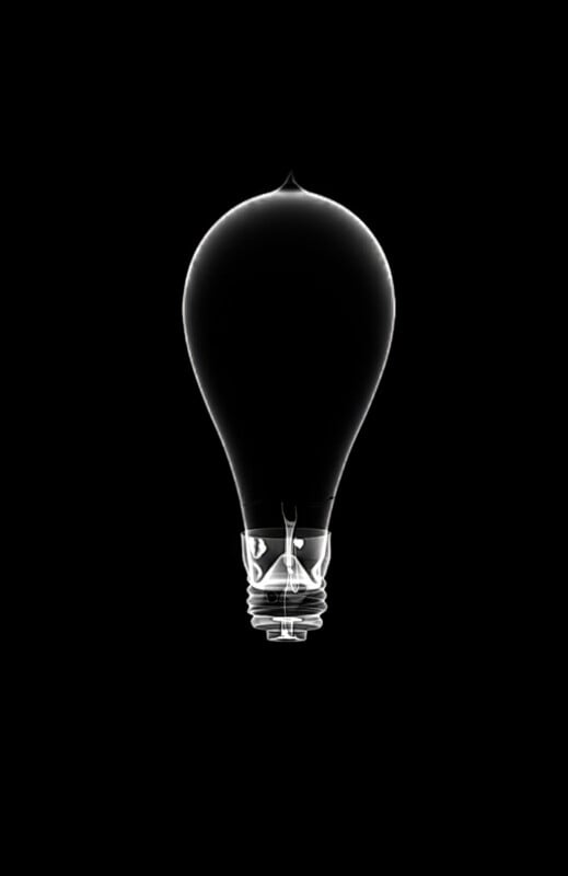 A transparent light bulb with a black interior is centered against a solid black background, creating a minimalist and striking contrast.