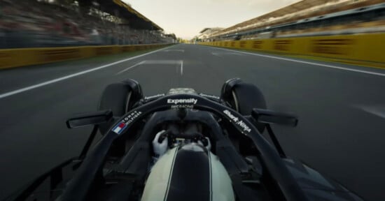 A view from behind the driver of a Formula 1 car racing down a straight track, with blurred grandstands and barriers on both sides, capturing a sense of speed and motion.