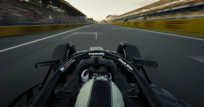 A view from behind the driver of a Formula 1 car racing down a straight track, with blurred grandstands and barriers on both sides, capturing a sense of speed and motion.