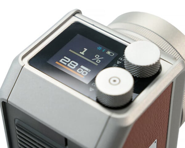 Close-up of a modern electronic device with two silver control knobs and a screen displaying "1%", a battery icon, a signal icon, and the number "28" with smaller numbers beside it. The device has a metallic and leather finish.