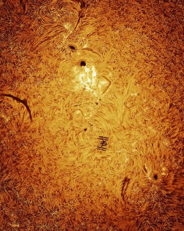 A detailed, close-up image of the Sun’s swirling, fiery surface shows sunspots and filamentary patterns, with the silhouette of the International Space Station crossing in front of the Sun.