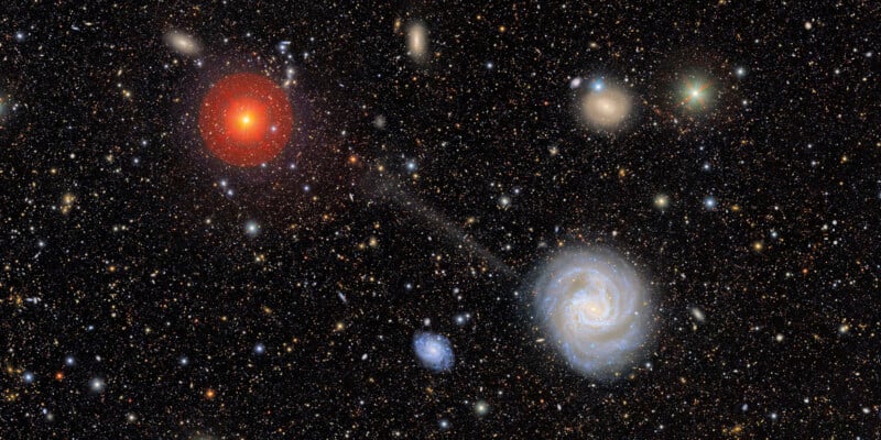 A star-filled galaxy image with a bright red star on the left, a spiral galaxy on the lower right, several smaller galaxies, and countless stars scattered across a dark space background.