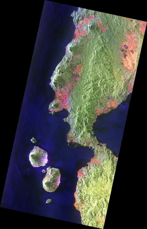 Satellite image of a coastal landmass with rugged green terrain and three small islands nearby, surrounded by dark blue ocean waters. The land and islands are highlighted in green, pink, and yellow tones.