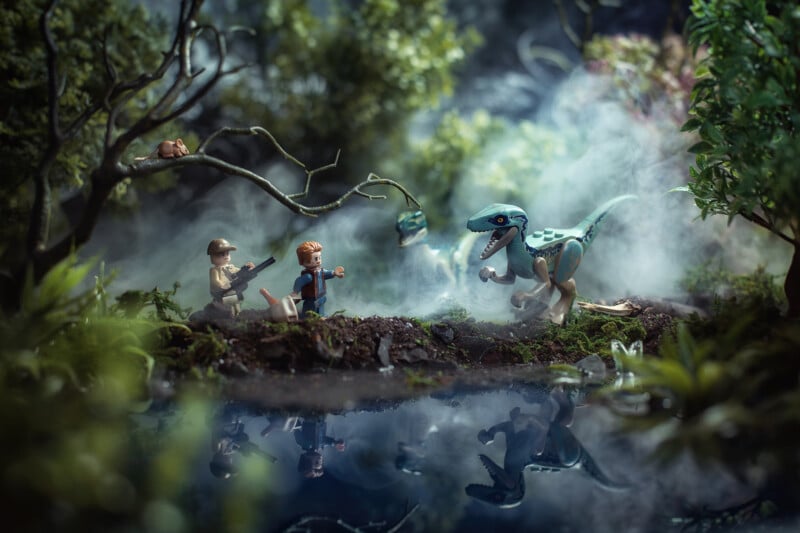 Two LEGO figures, one holding a gun, face a blue raptor dinosaur near a misty forest pond. Dense foliage and tree branches surround them, creating a dramatic, jungle-like scene.
