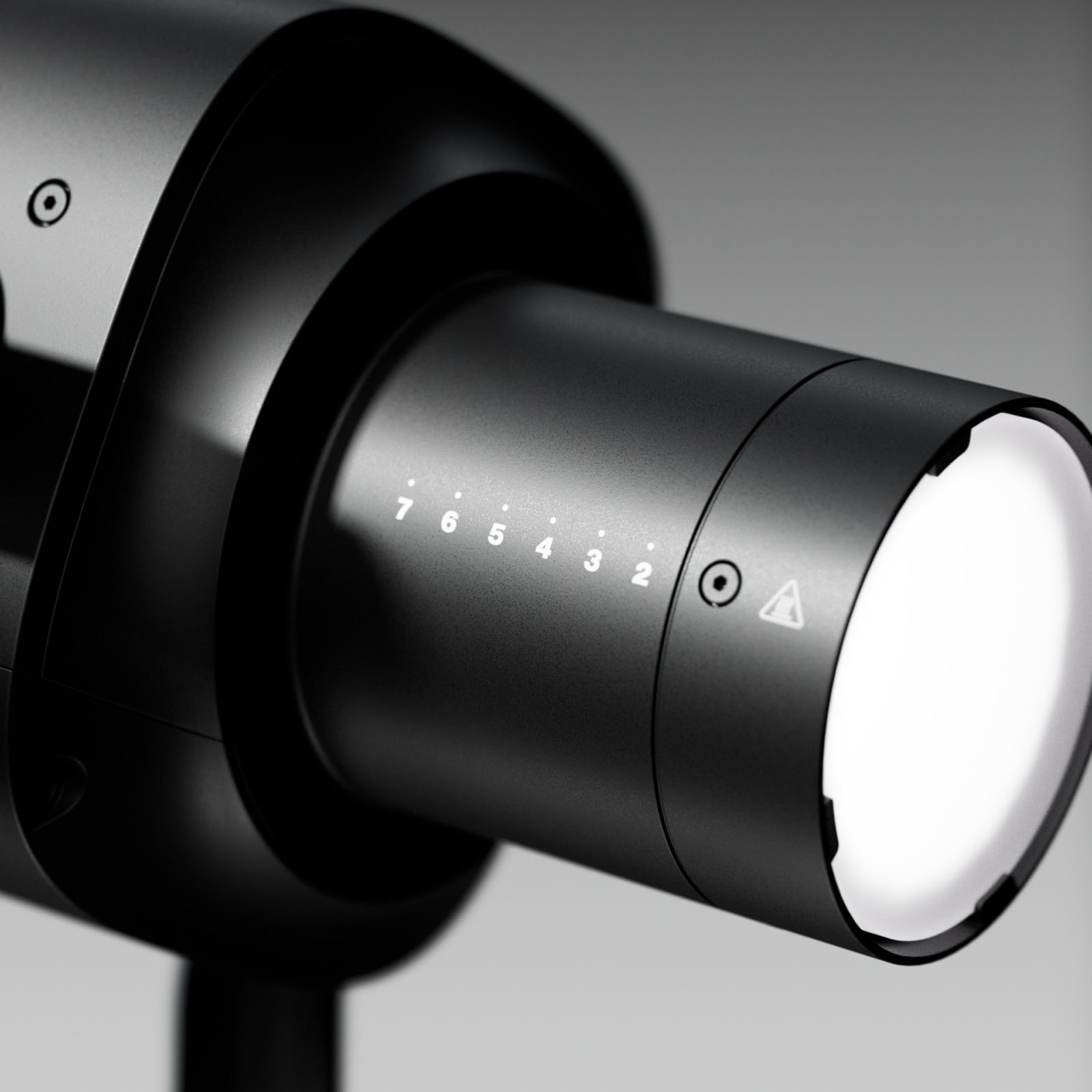 A close-up of a sleek, modern black device with a cylindrical lens and numbers 2 to 7 marked on its side, next to a caution symbol. The background is softly blurred in shades of gray.