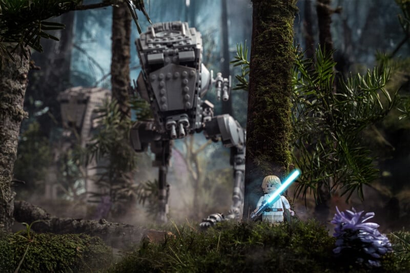 A LEGO figure with a blue lightsaber stands in a misty forest with dense trees and plants. Behind it, a LEGO AT-ST walker advances through the trees, evoking a Star Wars scene.