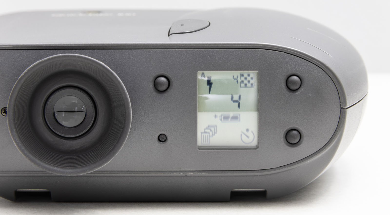 Close-up of a digital camera’s LCD screen displaying several icons, including a lightning bolt (flash), a chessboard pattern, a low battery indicator, and a power symbol, with the camera lens visible on the left.