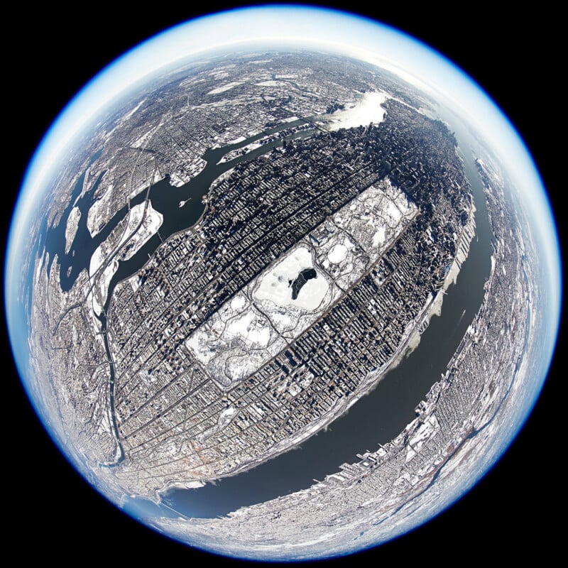 A fisheye aerial view of Manhattan, New York City, with Central Park covered in snow, surrounded by buildings and bordered by rivers on both sides under a blue-tinted sky.