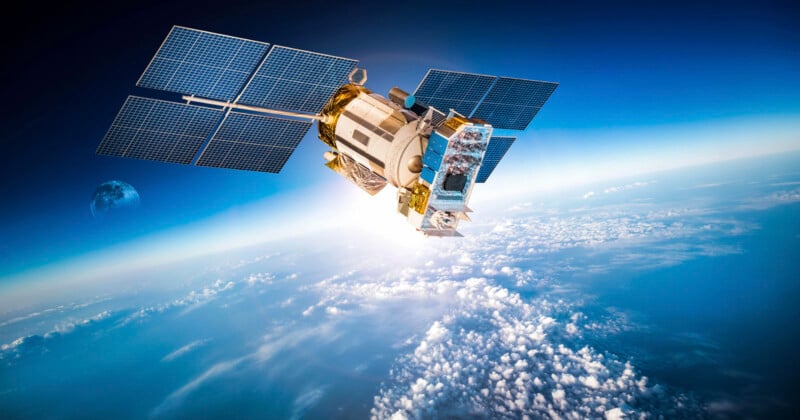 A satellite orbits above Earth’s atmosphere, with solar panels extended and clouds, the planet’s surface, and the Moon visible in the background.