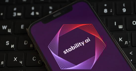 A smartphone displays the Stability.ai logo on its screen, featuring geometric lines in pink and red around the name. The phone rests on a black keyboard with Cyrillic and Latin characters.