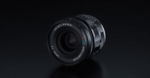 A Voigtländer APO-LANTHAR 35mm f/2 camera lens is displayed on a glossy black surface, showing its detailed engravings and multicolored logo markings near the front element.