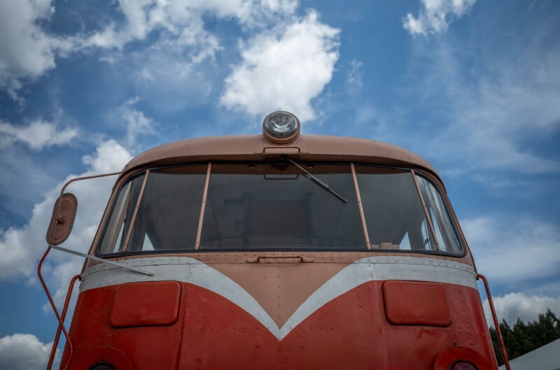 Front view of a vintage red and brown train engine with a single headlight, set against a bright blue sky with scattered white clouds.