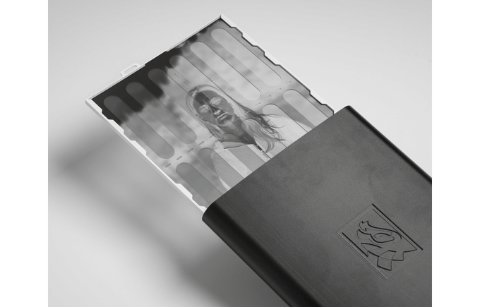 A black-and-white photo negative with an image of a woman is partially pulled out of a black plastic storage case on a white background.