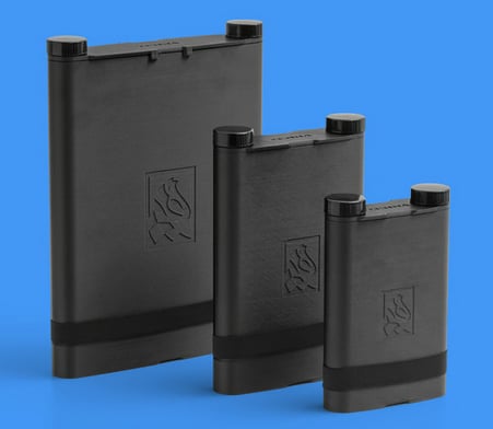 Three black rectangular canisters of varying heights stand upright on a blue background, each featuring a flame logo and two screw caps on top.