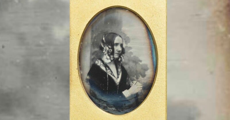 A sepia-toned portrait of a woman in Victorian-era clothing, with floral hair accessories, seated and looking to the side. The image is oval-shaped and framed in gold.