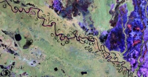 Colorful satellite image of a winding river with many oxbow bends, surrounded by green, blue, and purple textured terrain, showing distinct natural patterns and water bodies.