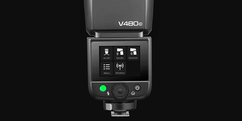 Close-up of a V480C camera flash unit showing its digital display and control buttons on a black background. The screen displays menu options for Wi-Fi, sender, receiver, and wireless mode.