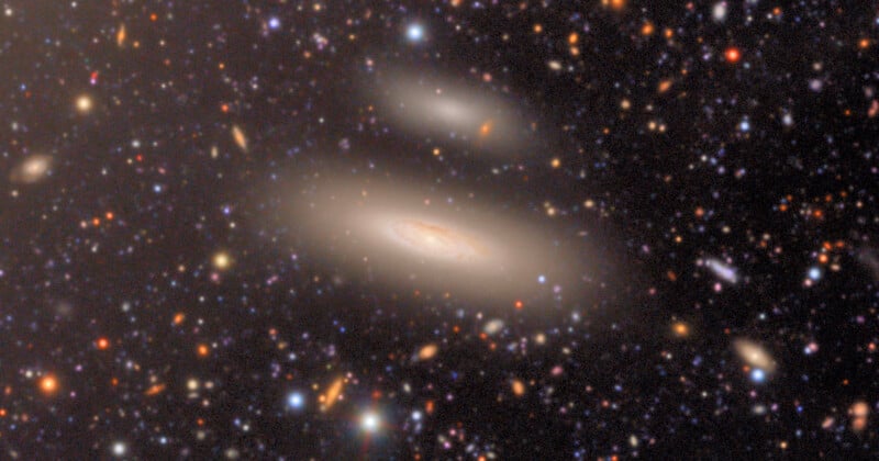 A bright spiral galaxy is surrounded by a faint halo, with many stars and distant galaxies scattered across the dark, star-filled background of space.
