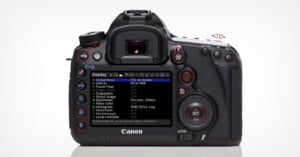 A Canon DSLR camera viewed from the back, displaying an on-screen settings menu labeled "Overlay" with various options such as Zebras, Focus Peak, and Histogram. Several buttons and dials are visible around the screen.