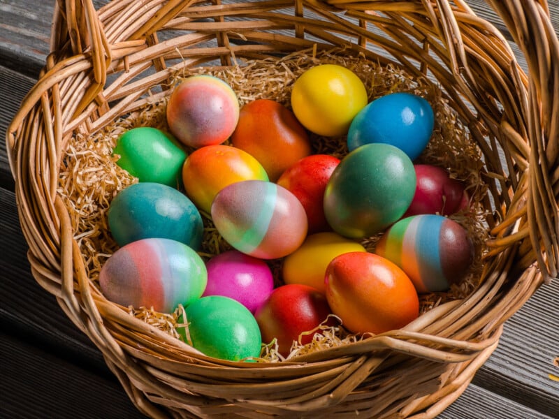 A wicker basket filled with colorful, decorated Easter eggs resting on straw, placed on a wooden surface.
