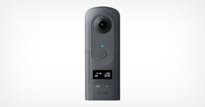 A black Ricoh Theta 360-degree camera stands upright against a plain white background, featuring a circular lens at the top, a blue indicator light, control buttons, and a small digital display on its front.