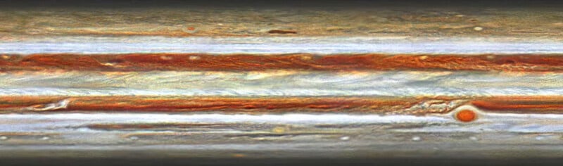 A stretched, horizontal view of Jupiter's colorful atmosphere, showing bands of swirling clouds in shades of white, orange, and brown, with the Great Red Spot visible on the right.