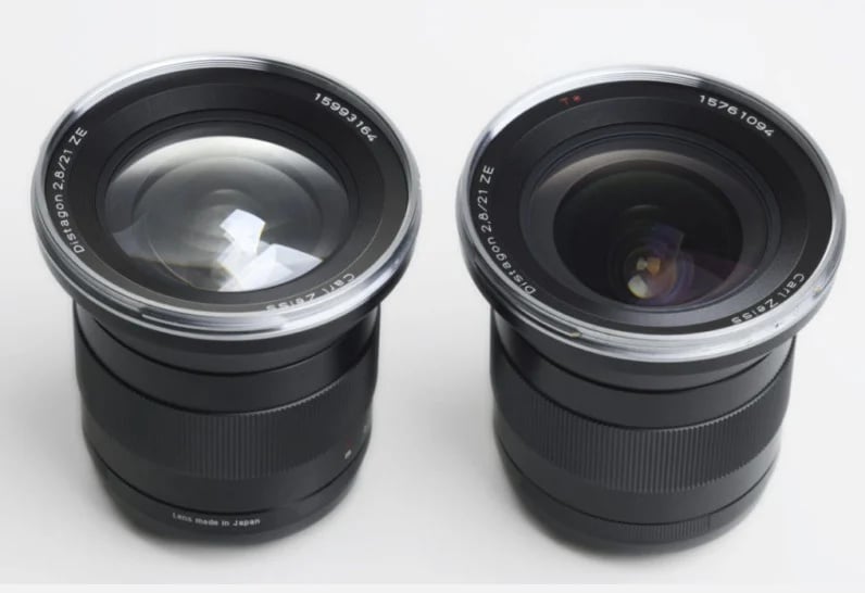 Two black camera lenses with rear lens caps removed are placed side by side on a white surface; both are labeled “Distagon 2.8/21 ZE” with visible glass elements facing upward.