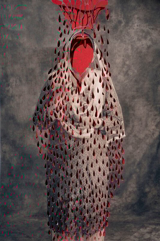 A veiled figure stands against a gray backdrop, covered by a mesh-like white fabric adorned with numerous red teardrop shapes, and a large red cutout above the head, creating a dramatic and surreal appearance.