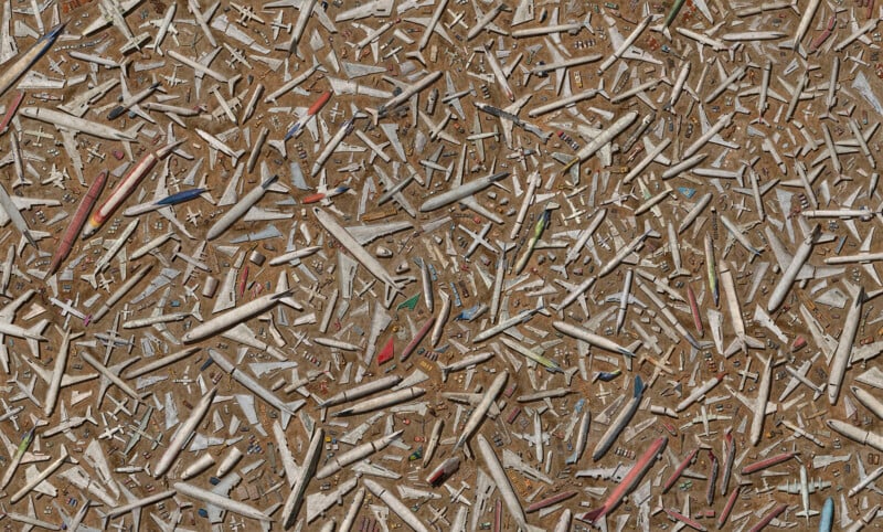 Aerial view of numerous abandoned airplane bodies and parts scattered across a dry, brown surface, creating a dense, chaotic pattern of fuselages, wings, and tails.