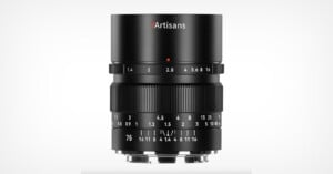 A black 7Artisans camera lens with manual focus and aperture rings, showing aperture and focus distance markings, standing upright on a white background.