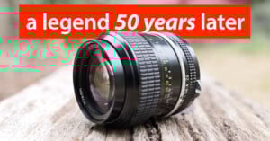 A Nikon camera lens rests on a weathered wooden surface outdoors with the text "a legend 50 years later" in bold red and white at the top of the image.