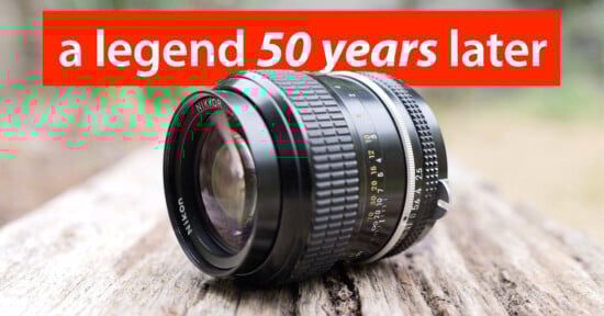 A Nikon camera lens rests on a weathered wooden surface outdoors with the text "a legend 50 years later" in bold red and white at the top of the image.