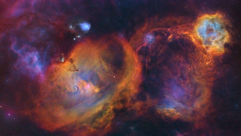 A vibrant image of a colorful nebula in space, featuring swirling clouds of orange, blue, purple, and red gas, with scattered bright stars against a dark background.