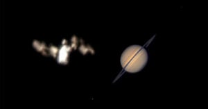 A blurry, bright object resembling the Bat-Signal appears on the left, while the planet Saturn with visible rings is clearly seen on the right, both set against a black background.