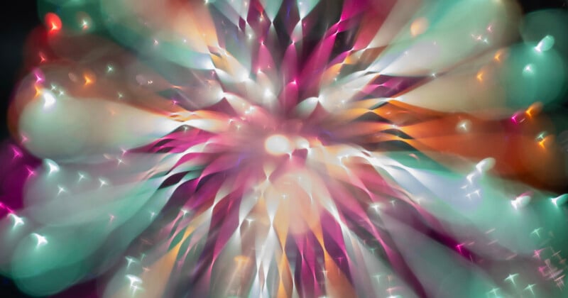 A vibrant, abstract burst of colors including teal, pink, orange, and white, radiating outward from a central bright point, resembling an explosion or a firework viewed through a soft, dreamy lens.