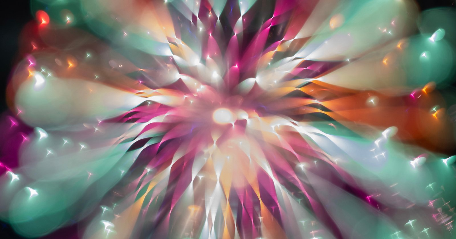 A vibrant, abstract burst of colors including teal, pink, orange, and white, radiating outward from a central bright point, resembling an explosion or a firework viewed through a soft, dreamy lens.