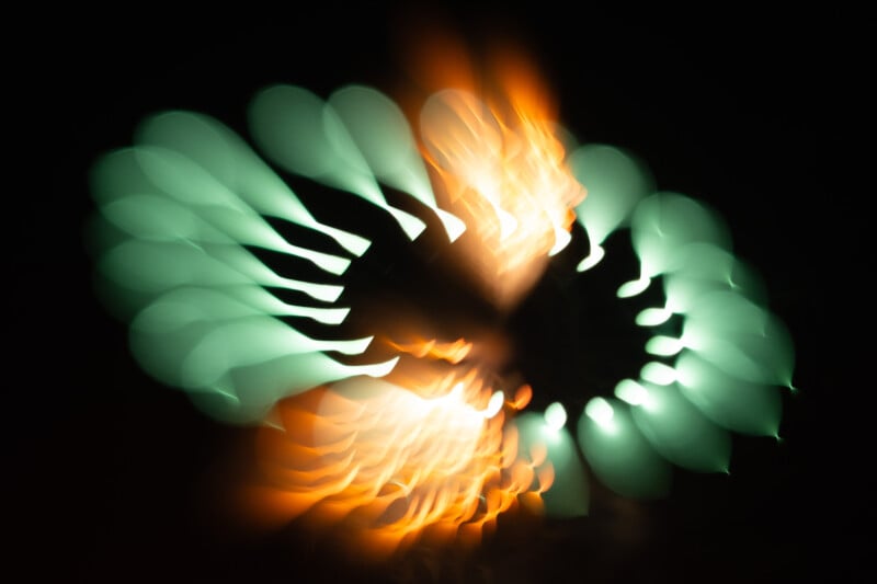 Abstract image with blurred teal and orange lights arranged in a circular pattern against a black background, creating a dynamic and glowing effect.