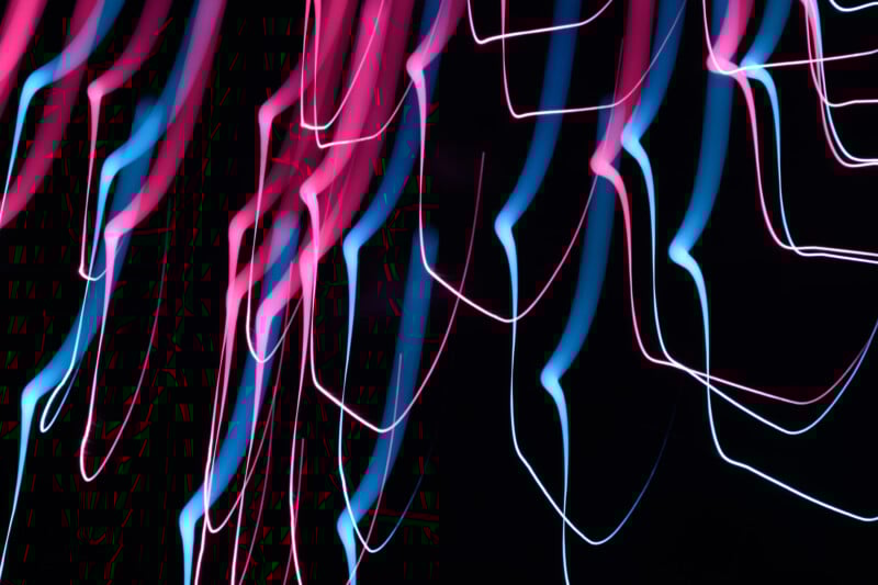 Abstract image of pink and blue light trails curving and zigzagging on a black background, creating a dynamic, neon effect.