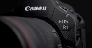 Close-up of a black Canon EOS R1 camera, showing the Canon brand logo and the model name “EOS R1” near the textured grip, with part of the lens visible on the left.