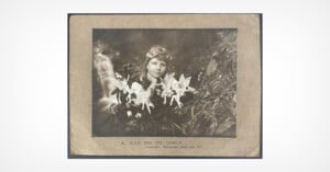 A vintage black-and-white photo of a girl outdoors with paper cutout fairies placed in front of her, blending into the natural background. The caption reads, "A Slide and the Fairies.