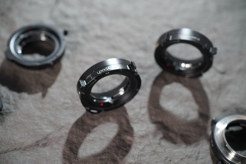 Close-up of several black camera lens adapters placed on a textured gray surface, with soft lighting creating shadows around the objects.