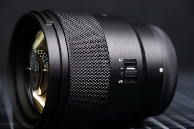 A close-up of a camera lens showing its textured focus ring and a switch for selecting between auto focus (AF) and manual focus (MF), set against a dark, blurred background.