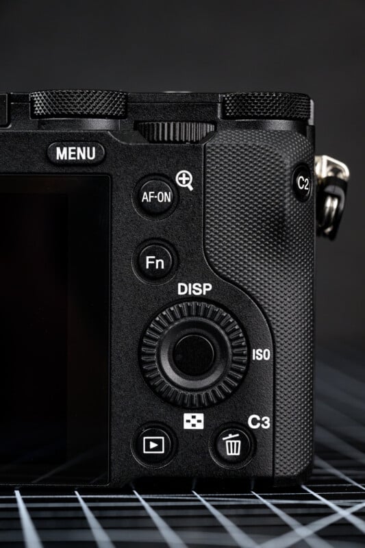 Close-up of the back right side of a digital camera showing buttons labeled MENU, AF-ON, Fn, DISP, ISO, C2, C3, and a control dial, with a textured grip and part of the LCD screen visible.