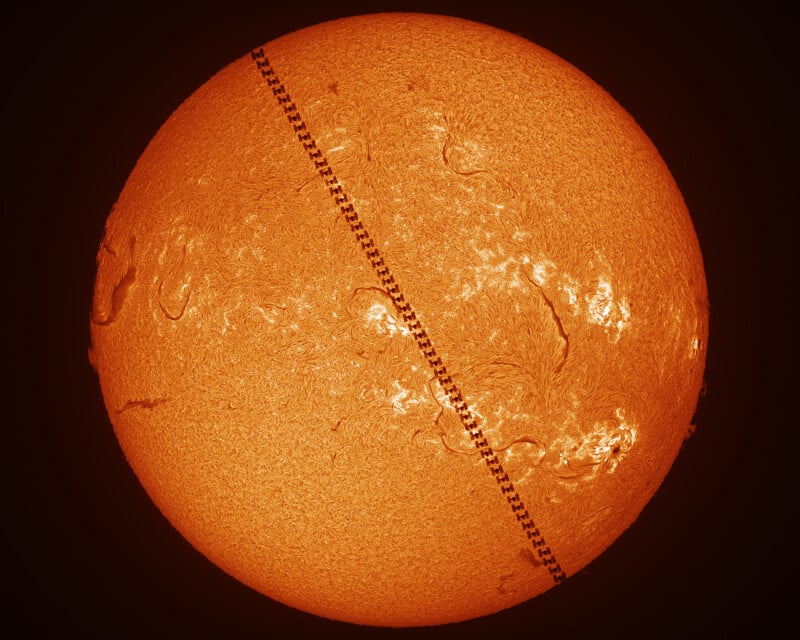 An orange, detailed image of the Sun with a dotted, diagonal black line crossing it, representing the silhouette of the International Space Station transiting in front of the Sun.