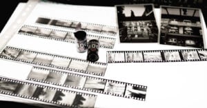 Black and white photo negatives, film canisters, and two printed photographs are displayed on a lightbox, showcasing various urban and landscape scenes.