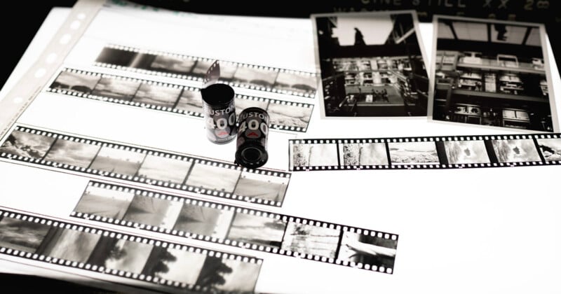 Black and white photo negatives, film canisters, and two printed photographs are displayed on a lightbox, showcasing various urban and landscape scenes.