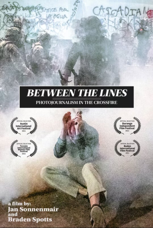 A person sits on the ground, covering their face amid tear gas as armed police in riot gear advance. Graffiti is visible on a wall behind them. The movie title "Between the Lines" and festival awards are overlaid on the image.