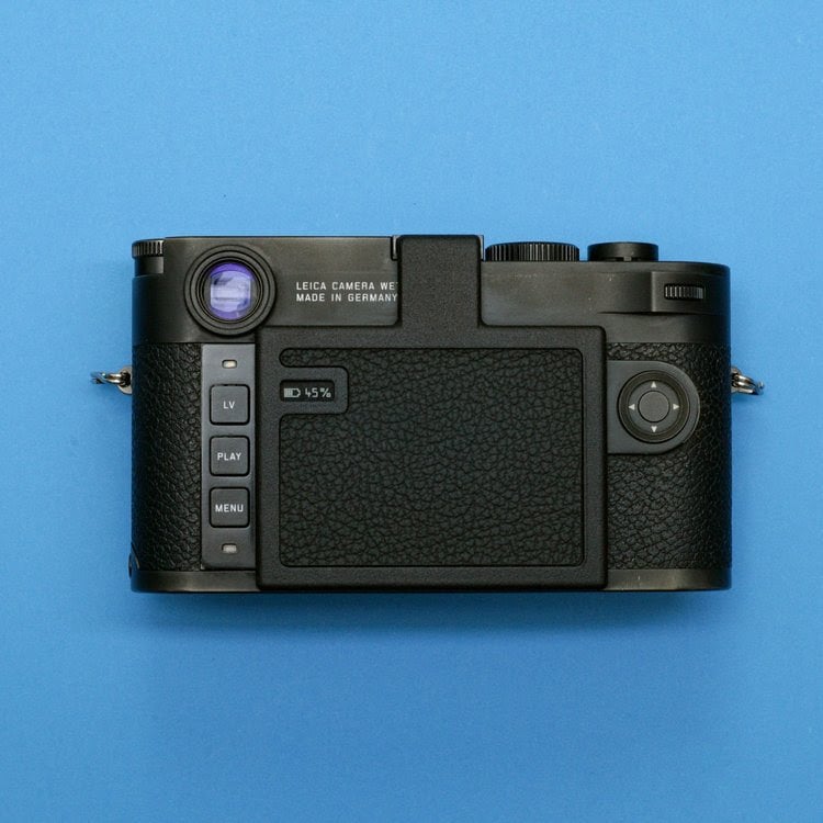 A black digital camera viewed from the back, showing buttons labeled LV, PLAY, MENU, and a small screen, set against a solid blue background.